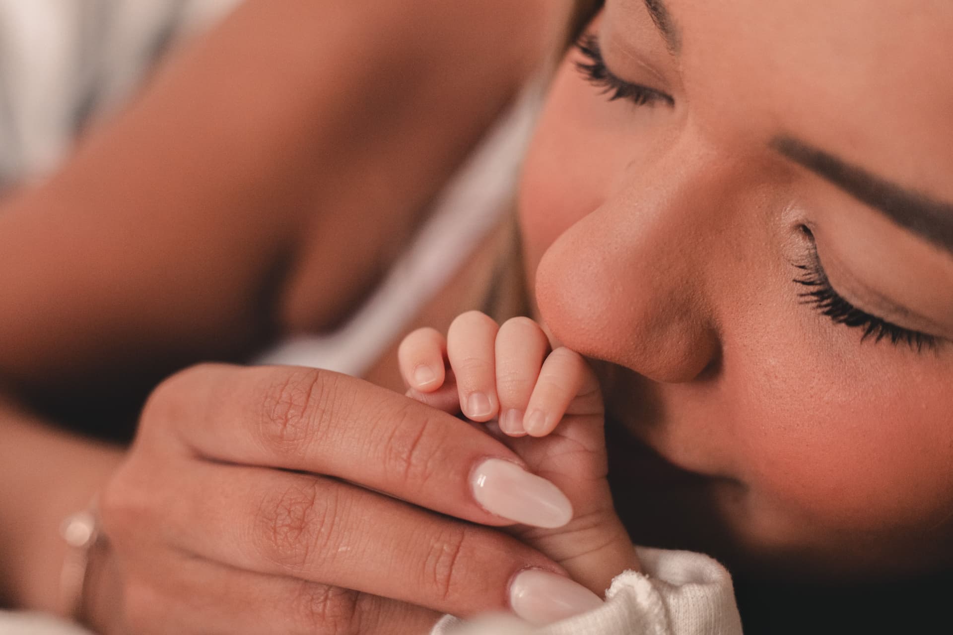 A mother gently kissing her newborn baby's tiny hand